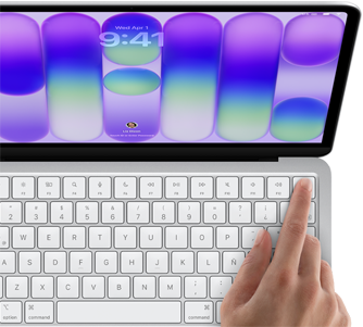 MacBook Neo, color plata, muestra la pantalla de inicio de sesión, el dedo de una persona en el sensor de Touch ID en la esquina superior derecha del teclado